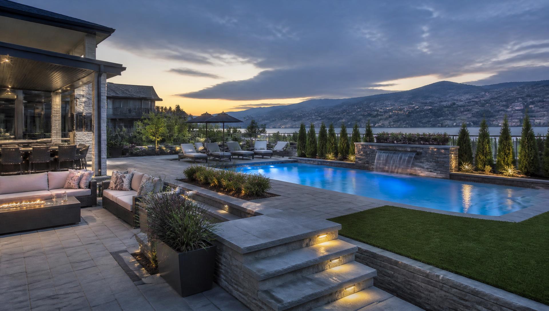 Paver pool deck and outdoor living space overlooking an Okanagan lake at dusk